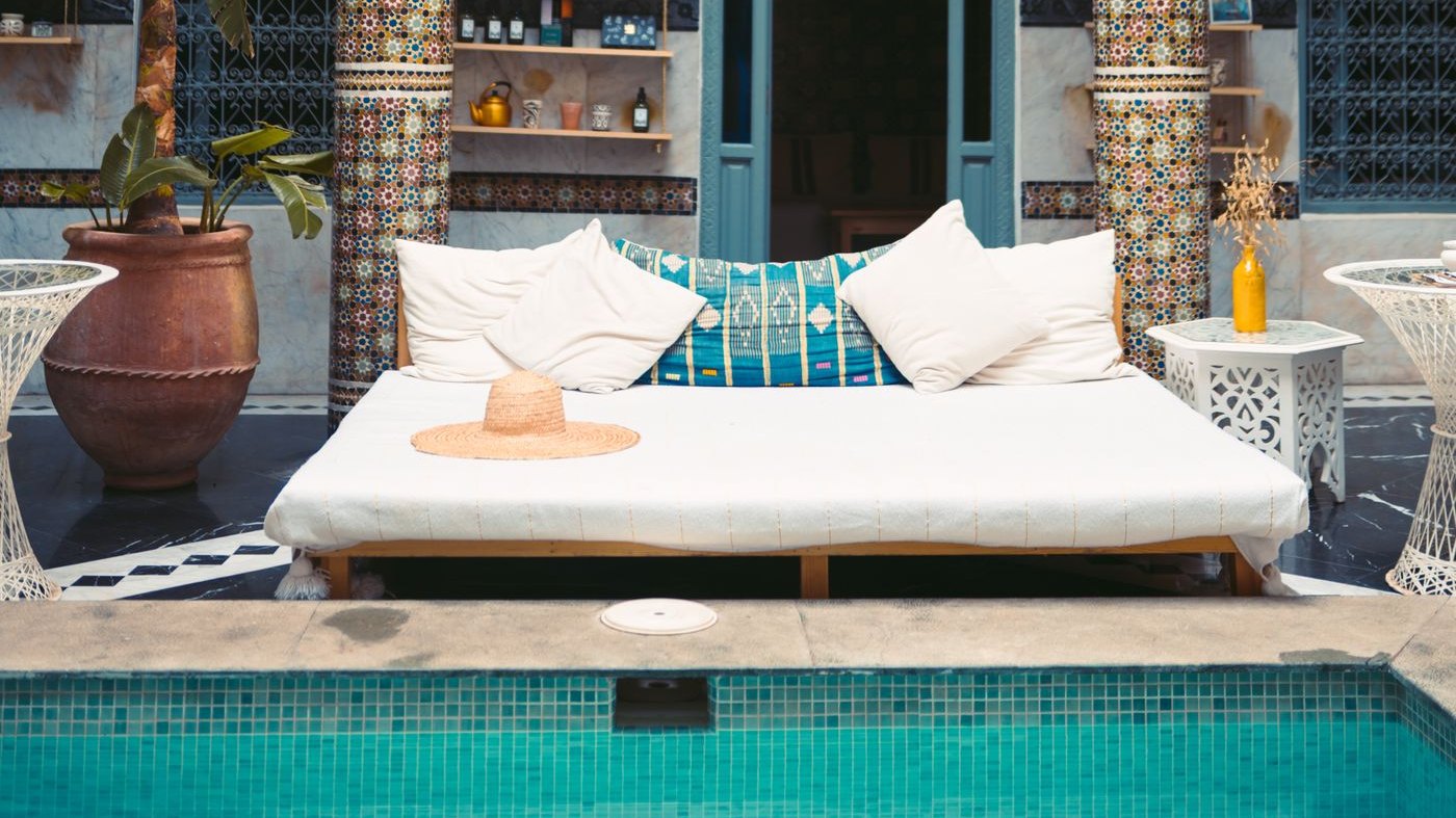 Patio d'un riad à Marrakech : piscine turquoise, banquettes blanches et colonnes en zellige